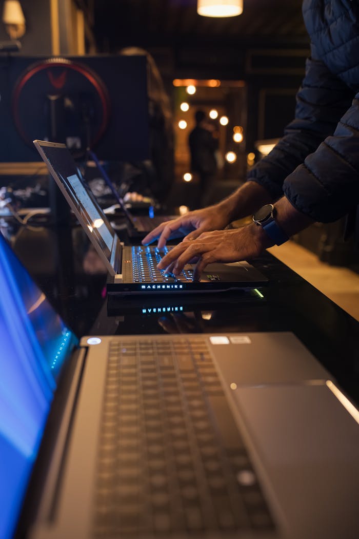 An individual typing on a laptop in a dimly lit modern workspace, emphasizing technology and focus.