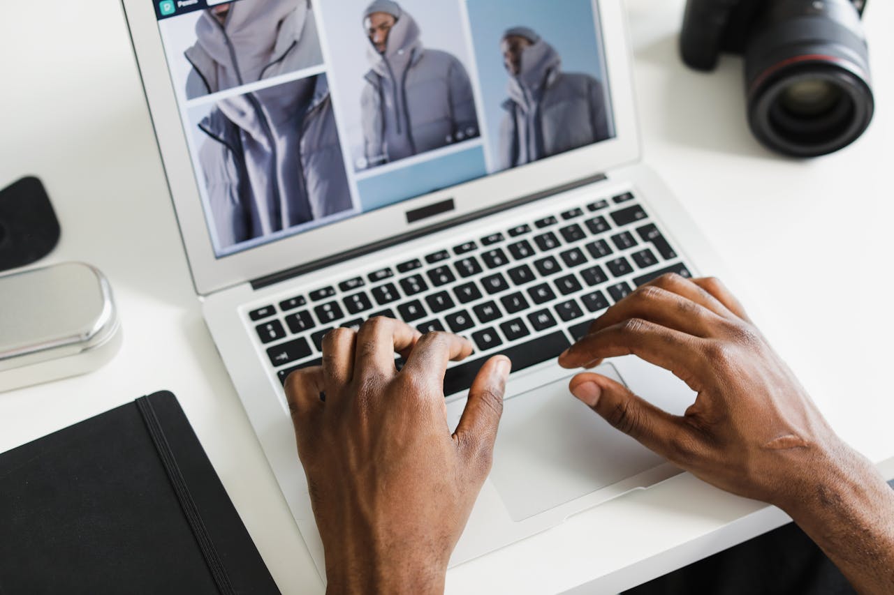 our-experience Close-up of hands typing on a laptop displaying a fashion website with a camera nearby.